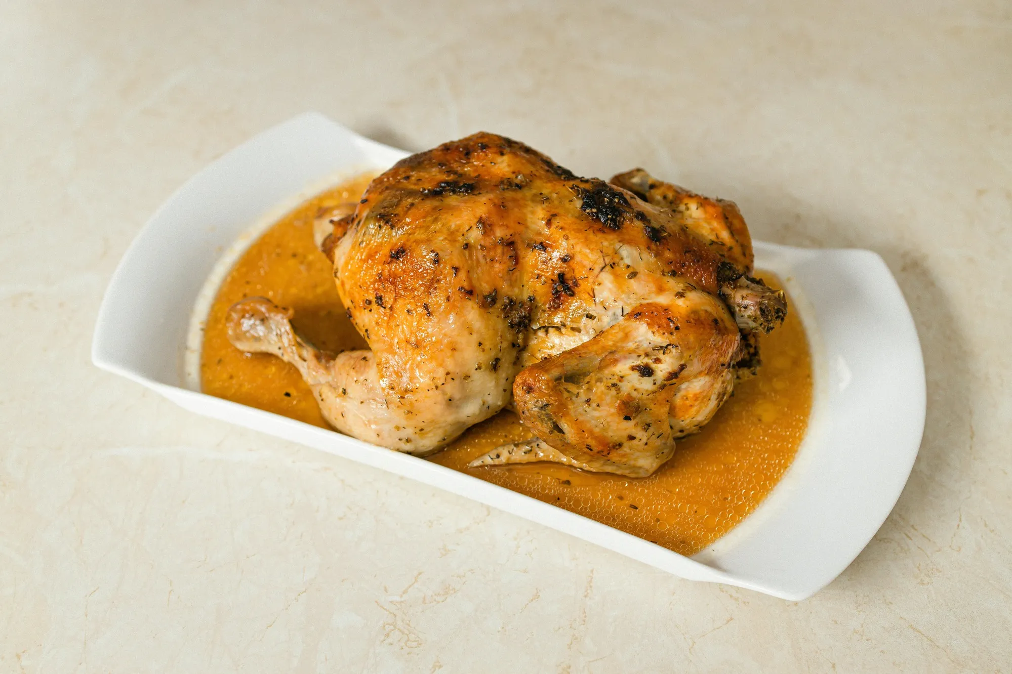 French chicken in a pot served whole with golden skin and rich jus on a white dish
