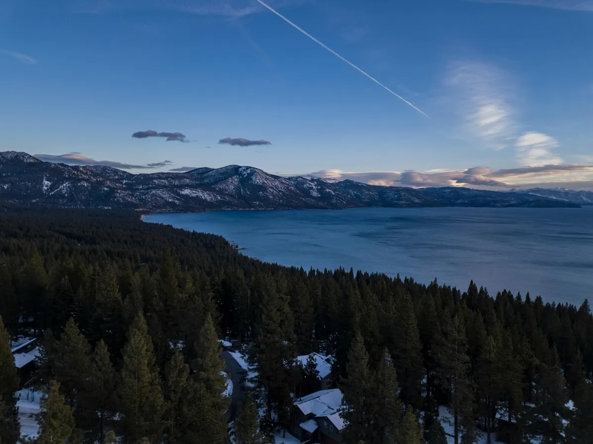 Aerial view of a mountain lake bordered by forest and snow-covered peaks at dusk