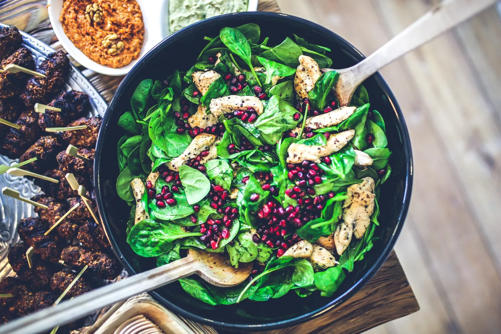 Bowl of spinach salad with sliced chicken and pomegranate seeds