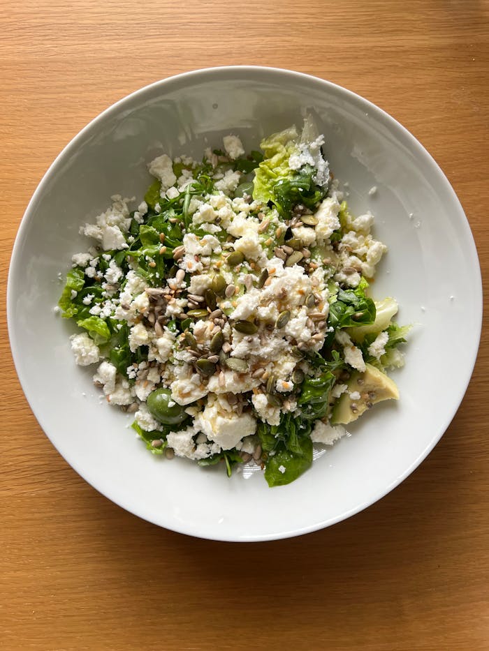 Delicious Greek salad with feta, avocado, and seeds on a wooden table.