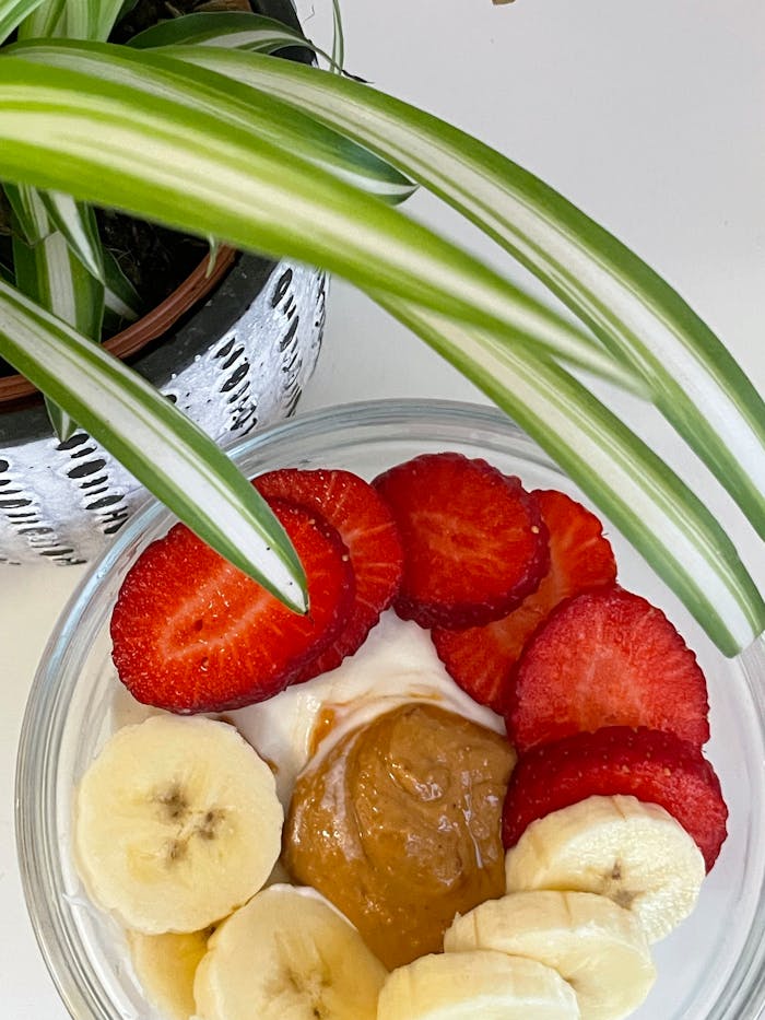 A delicious bowl of yogurt topped with bananas, strawberries, and peanut butter, accompanied by a potted plant.