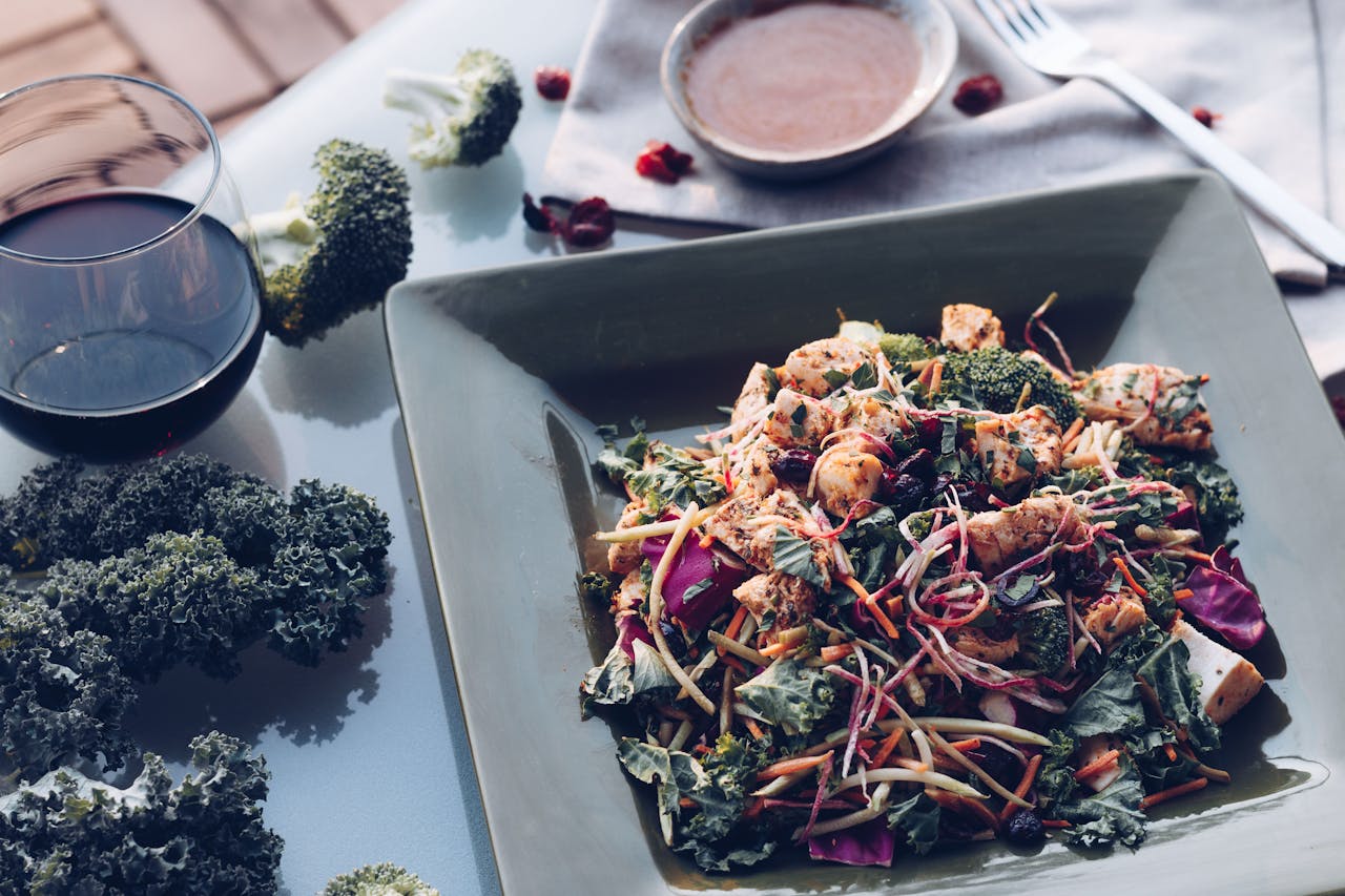 Delicious grilled chicken salad with kale, broccoli, and wine on a stylish table setting.
